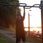 A man working out on pull-up bars in a park during sunset, capturing a healthy and active lifestyle.